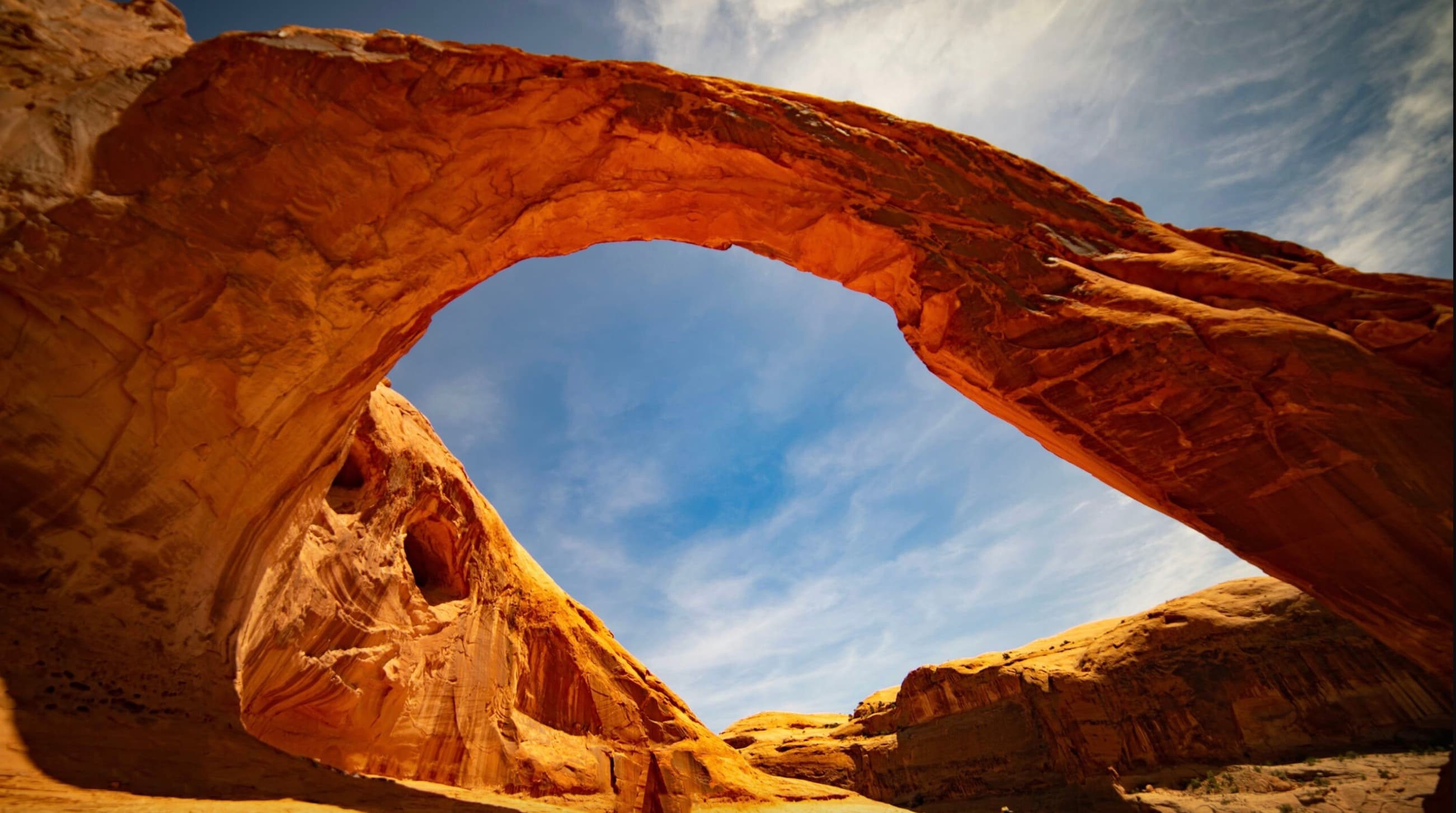 A sandstone natural arch in Utah's high desert, photographed from below against a blue sky.